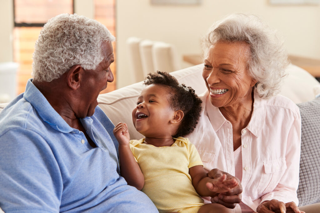 darker skinned person in blue shirt with short white hair sitting on sofa with young child in yellow shirt and older person with long white hair learning reasons grandparents can file for custody of a grandchild