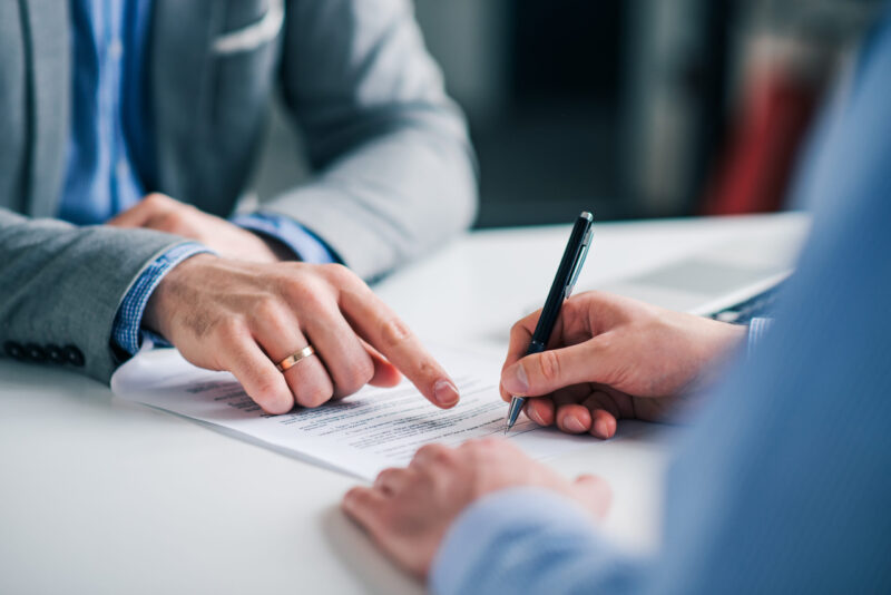 man in suit with wedding ring shows man in suit where to sign document and what is a promissory note
