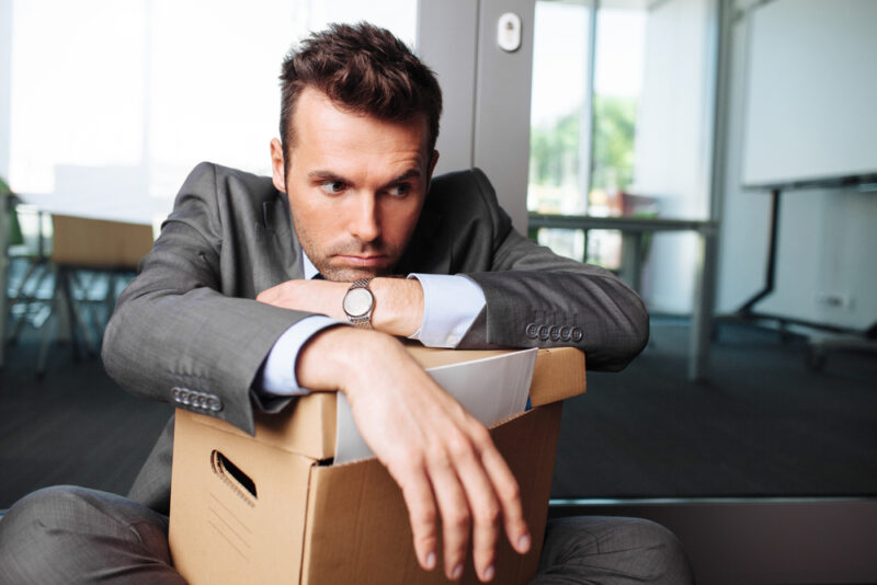 A man looks dejected and sad as he slumps over his box of office stuff after being fired from his job.